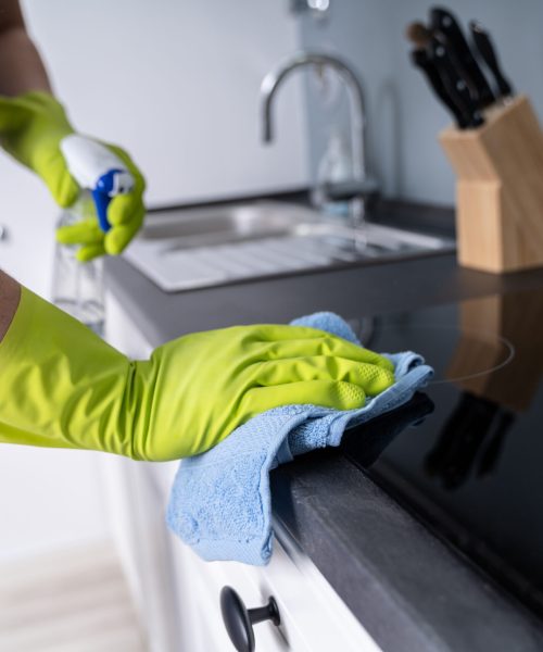 Midsection Of Male Janitor Cleaning Kitchen Counter With Detergent Spray Bottle And Sponge